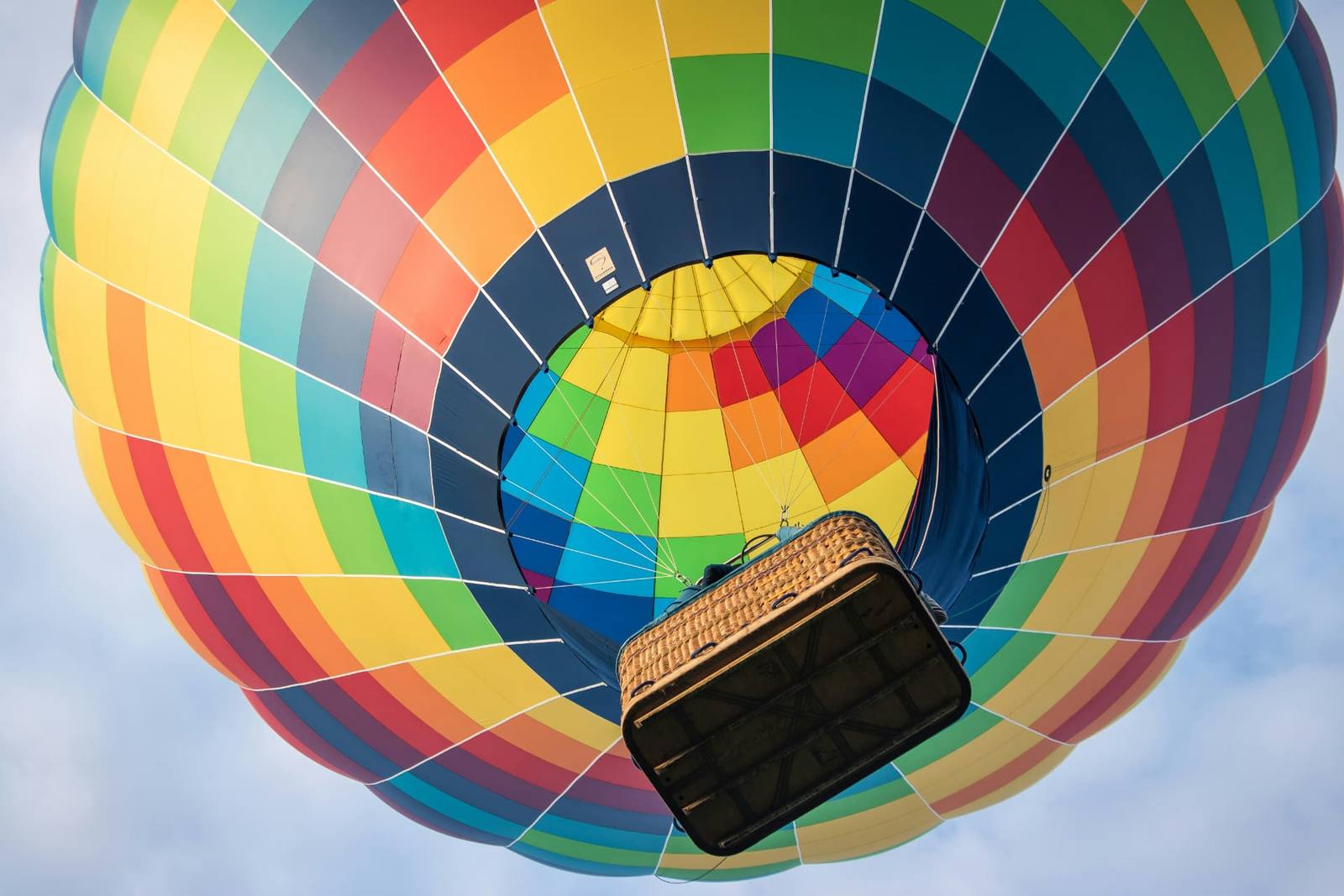 A vibrant rainbow hot air balloon ascending against a pale blue sky