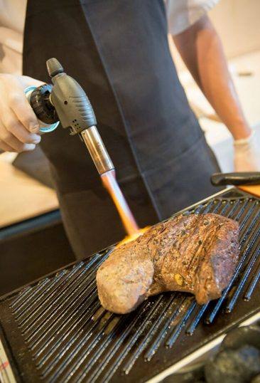 A chef searing a steak with a torch during a private culinary experience