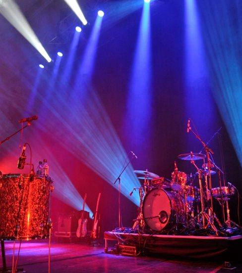 A concert stage with drum kit lit by blue and red stage lighting