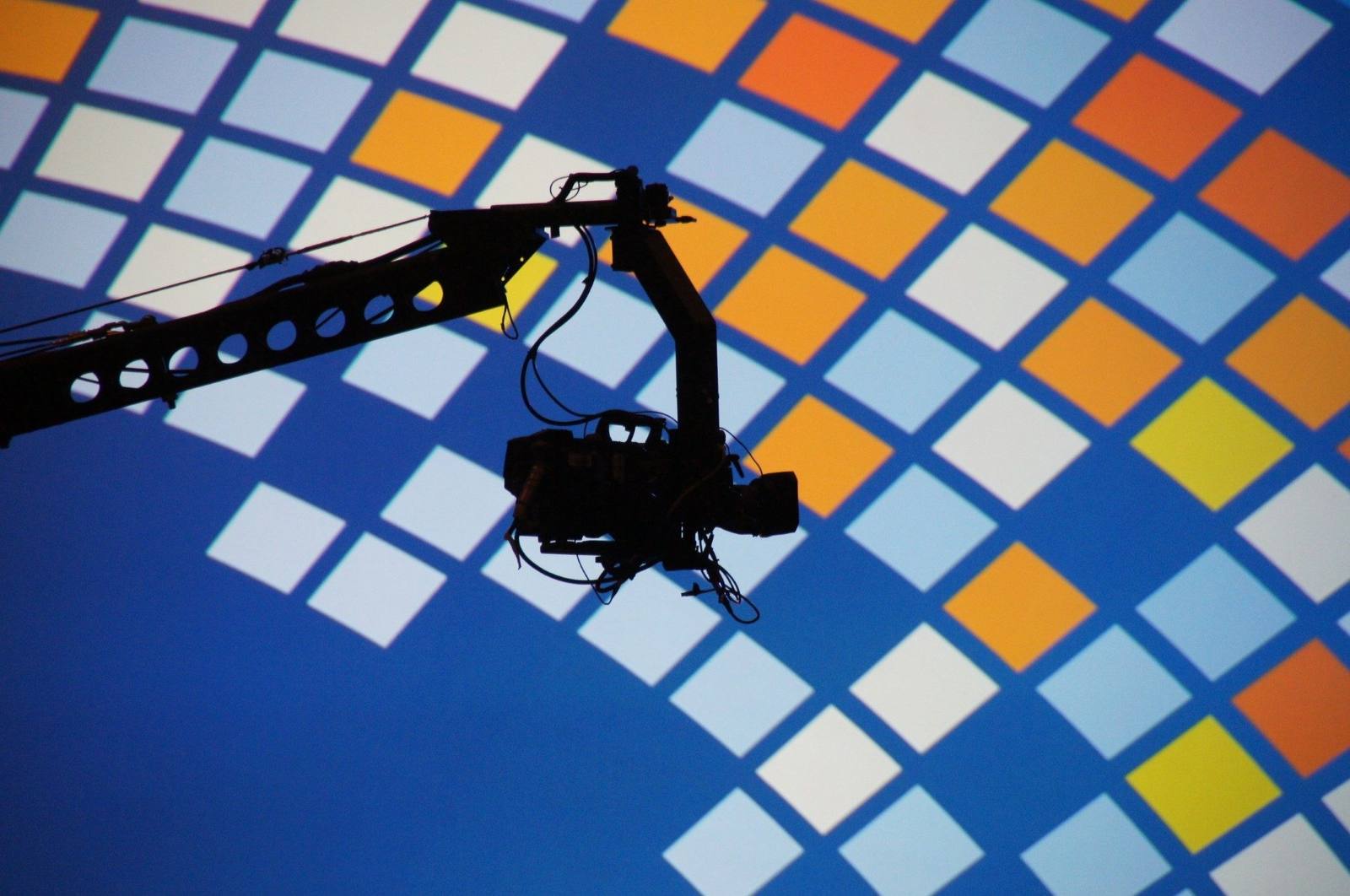 Professional event production camera crane silhouetted against a colorful stage grid