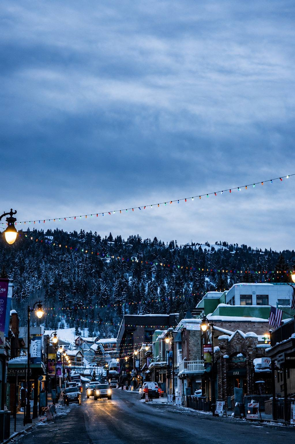 A snowy Park City street at dusk with string lights hanging above the road