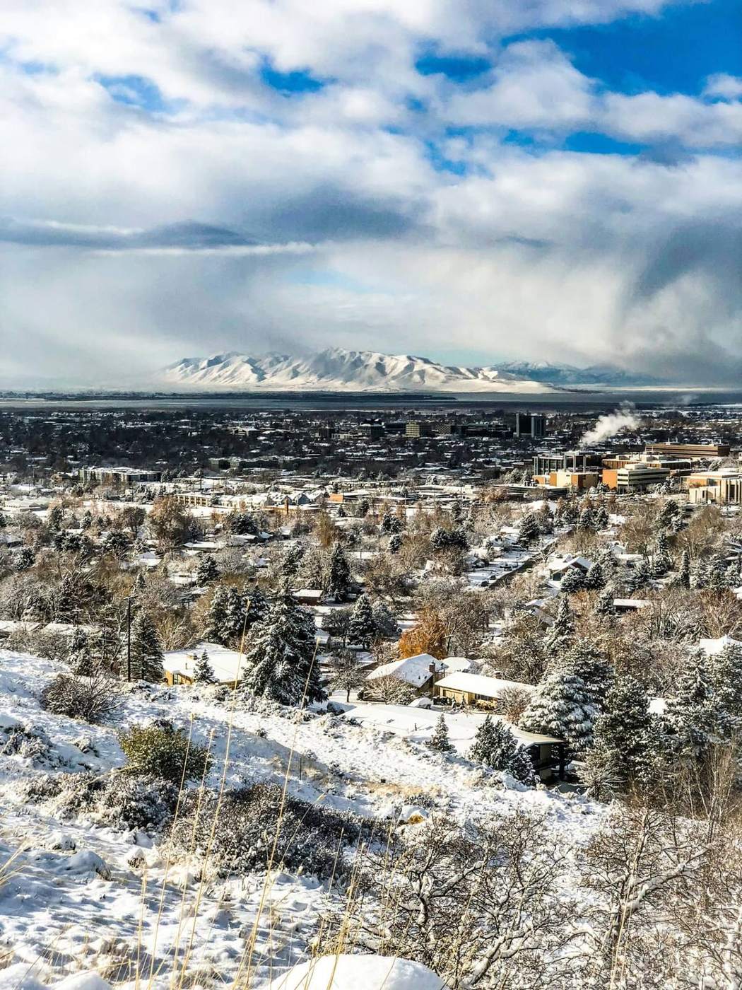 Snowy Wasatch Front cityscape with the snow-covered Wasatch Mountains rising under a partly cloudy sky